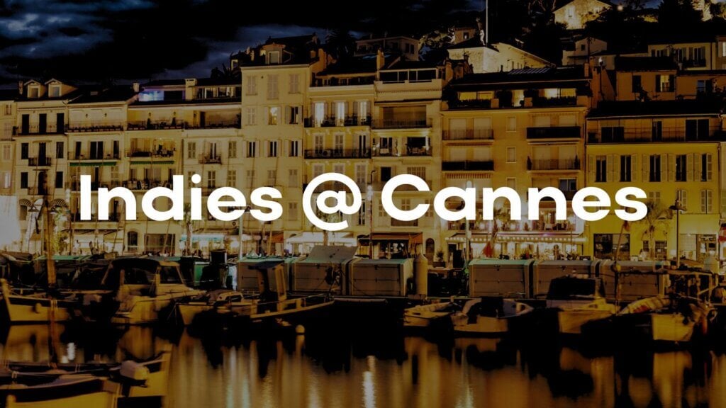 Night view of the Cannes harbor with illuminated buildings and boats, overlaid with bold white text reading Indies @ Cannes.