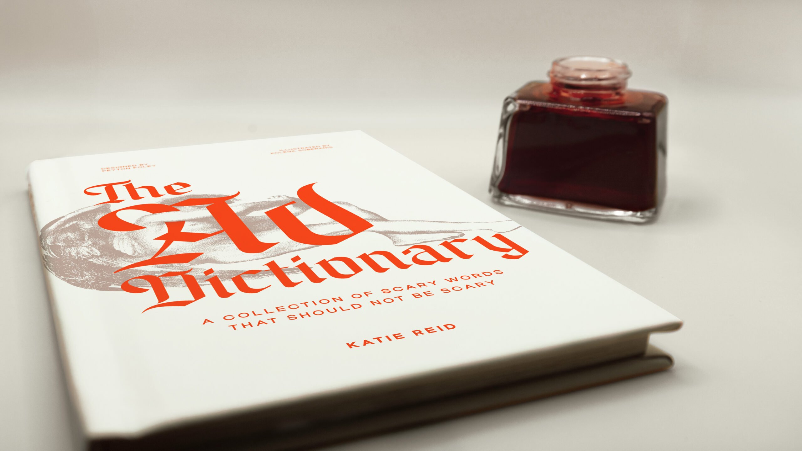 A hardcover book titled The Ad Dictionary, perfect for decoding Ad jargon or inspiring new talent, lies next to a square bottle of red ink on a light surface.