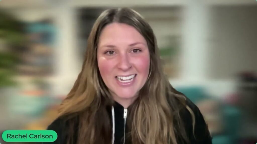 A woman with long brown hair smiles at the camera. She is wearing a black zip-up top and is indoors with a blurred background. The text Rachel Carlson, who shares tips on starting your own agency, appears in a green box.