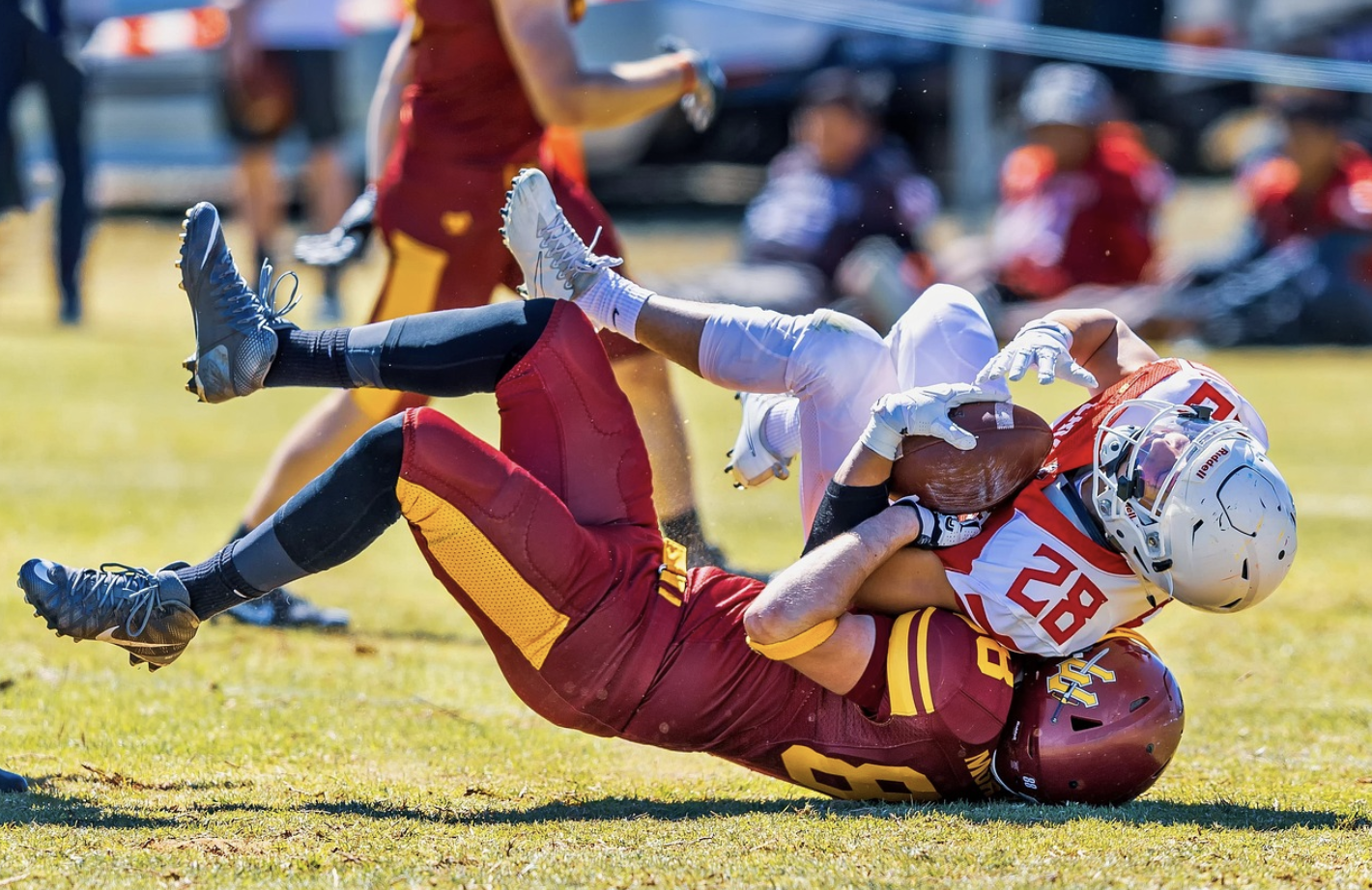 A football player in a maroon uniform tackles a player in white and red, bringing him down to the field—a dramatic moment that echoes the intensity seen in Super Bowl Sermons.