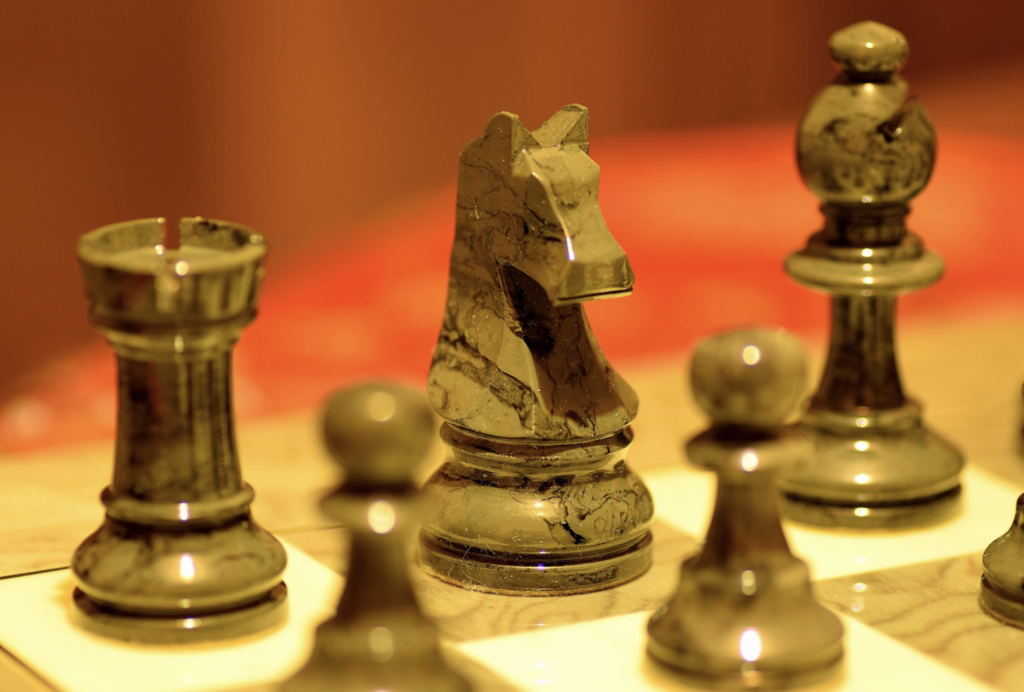 A close-up of carved black chess pieces, including a knight, rook, bishop, and pawns, positioned on a chessboard.