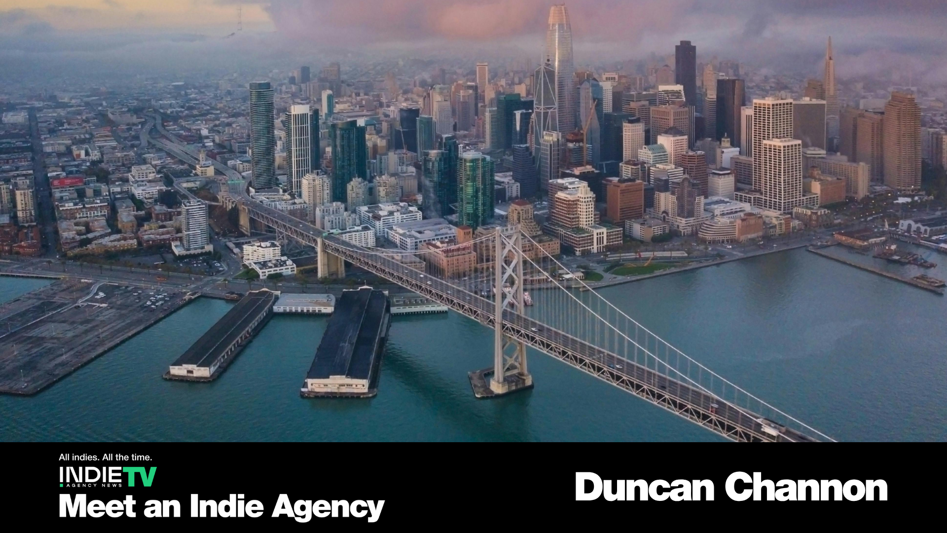 Aerial view of San Francisco skyline with the Bay Bridge in the foreground at sunset; text overlay promotes Duncan Channon agency and Indie TV.