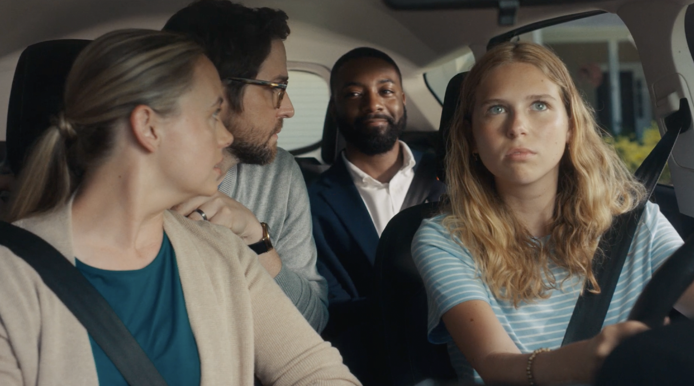 Four adults sit in a car. The woman in the driver’s seat looks ahead, while the other three passengers look at her. Everyone appears serious or contemplative, as if they’re pondering an important decision—perhaps inspired by a no-nonsense banking approach, much like First Interstate Bank highlights in their straightforward financial ads.