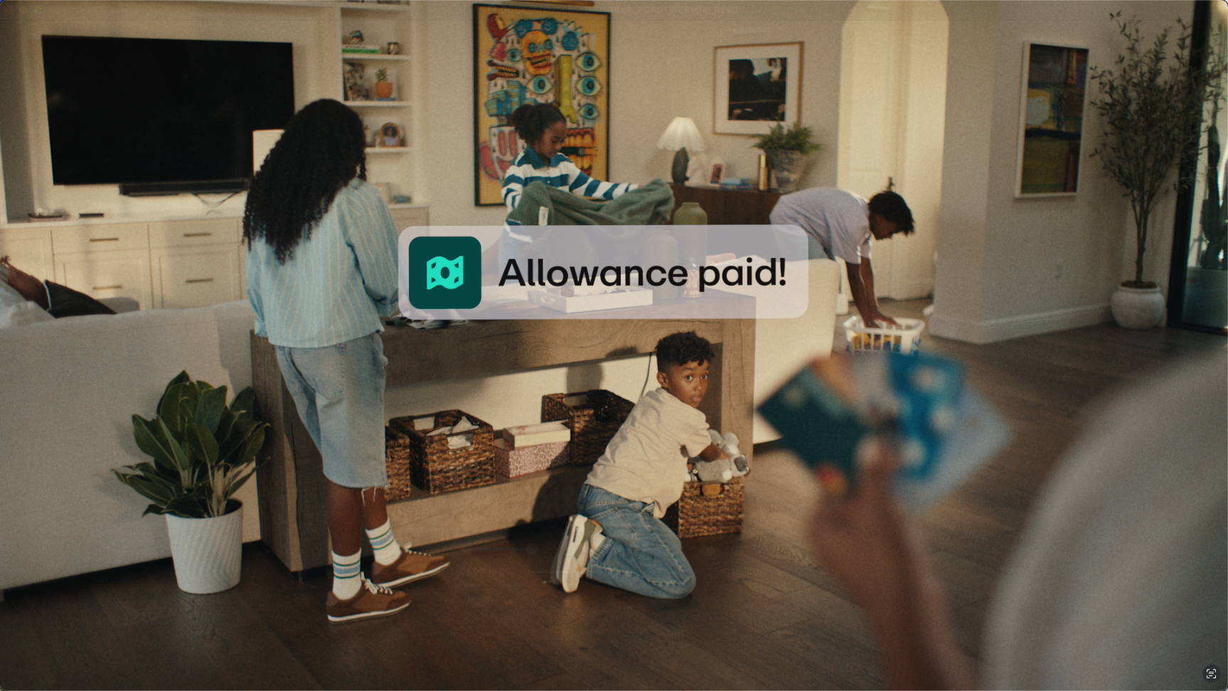 Four children in a living room, some looking through baskets amidst the typical family chaos, with a notification overlay that reads Allowance paid! on the screen.