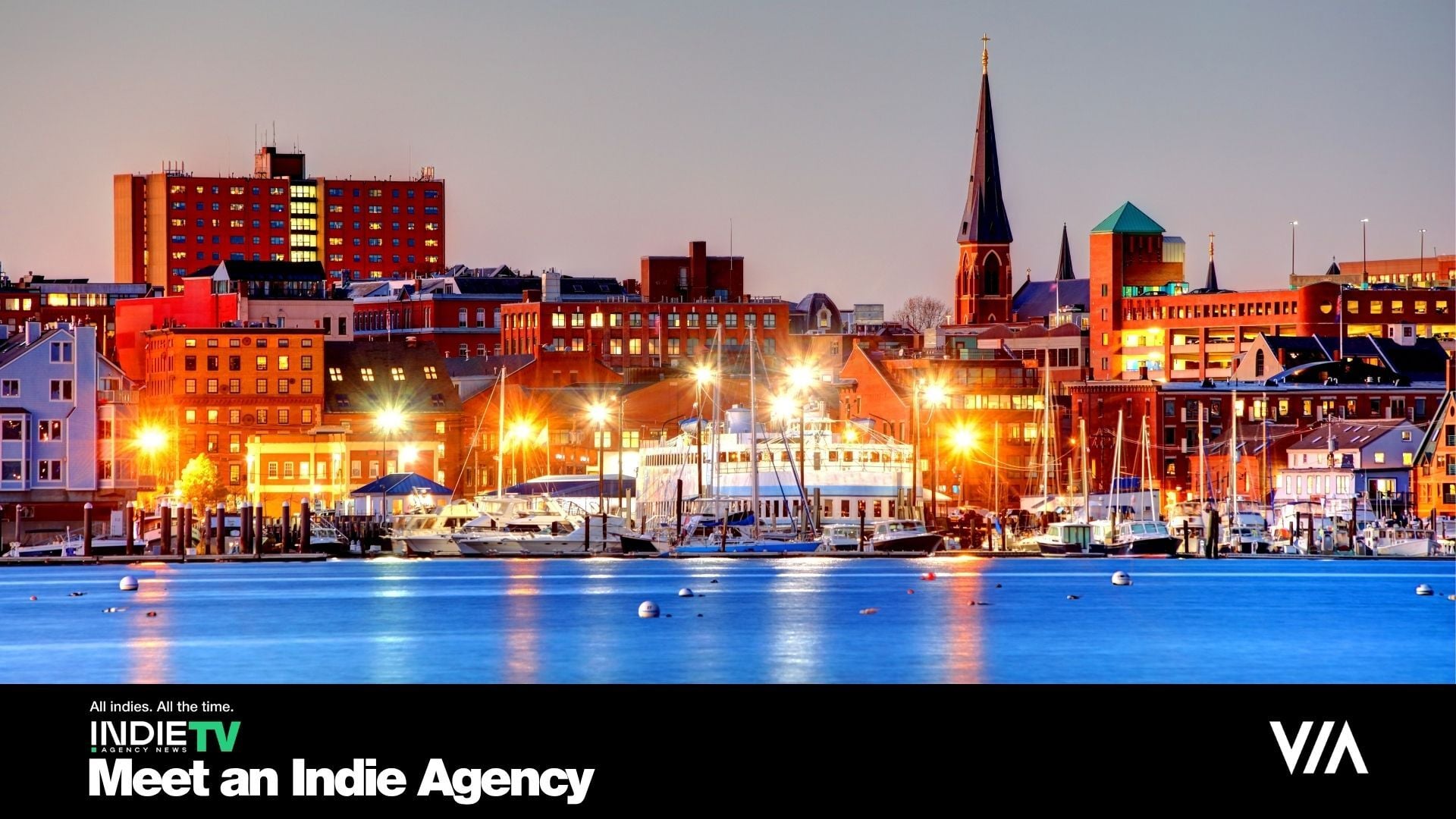 Portland city waterfront at dusk with boats docked in a marina, illuminated buildings, and a church steeple in the background—where creativity meets inspiration. Step into the Hogwarts of Advertising and see how indie talent comes together to decorate the world. Text overlay: Meet an Indie Agency and INDIE TV.