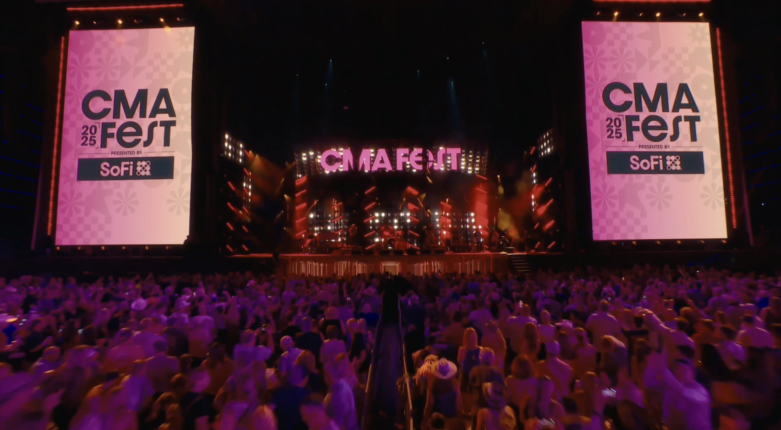A large crowd faces a brightly lit Nashville concert stage displaying the CMA Fest 2025 logo on two vertical side screens and a central archway, capturing the vibrant soundscape.